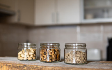 Sunflower seeds, walnut and almond in a jars which standing on a white vintage table with a kitchen on background. Nuts is a healthy vegetarian protein and nutritious food. Nuts on rustic old wood.