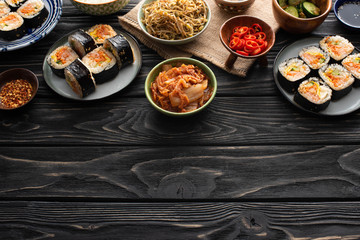plates with fresh gimbap near korean side dishes on wooden surface