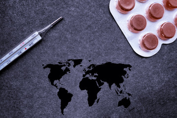 Top view on thermometer, pills and dark world map on gray black background. Virus, pademia in the world