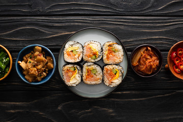 top view of plate with gimbap near side dishes in bowls on wooden surface
