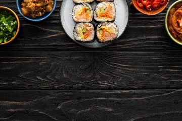 top view of plate with tasty gimbap near side dishes in bowls on wooden surface
