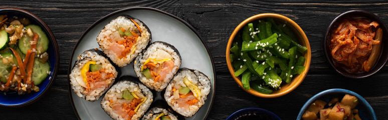 panoramic shot of korean gimbap near side dishes on wooden surface