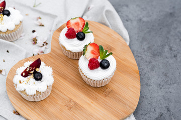 Vegan cupcakes with berries and coconut cream on a wooden board.