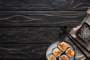 top view of chopsticks and sesame oil near plate with tasty rice rolls on wooden surface