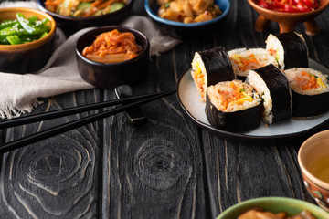 selective focus of delicious gimbap near korean side dishes and cotton napkin on wooden surface