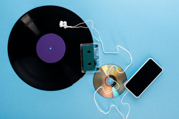 top view of vinyl record, compact disk, earphones, audio tape and smartphone with blank screen on...