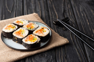 selective focus of tasty gimbap with vegetables and salmon near chopsticks on wooden surface