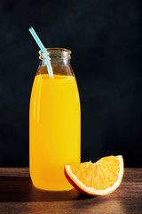 range juice in a glass bottle with straw and an orange slice on wooden table