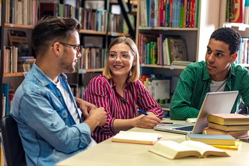 Three young students study in the school library and using laptop for researching online.