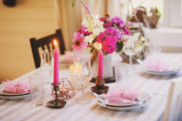 summer festive table setting in beautiful country house. Table decorated with pink flowers and candles.