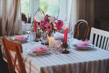 Evening dinner at home. Summer festive table setting in beautiful country house. Table decorated with pink flowers and candles.