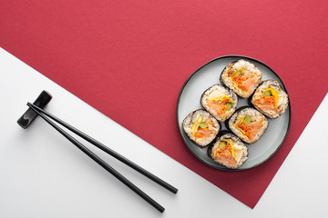 top view of chopsticks near plate with gimbap on white and crimson