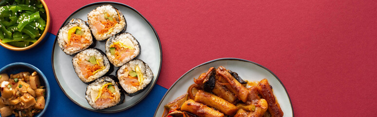 panoramic shot of plates with tasty gimbap near korean side dishes on blue and crimson