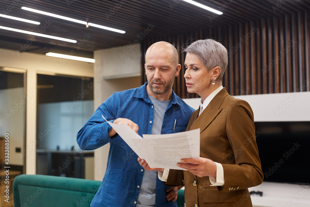 Wall mural waist up portrait of modern mature businesswoman discussing documents with colleague or client while