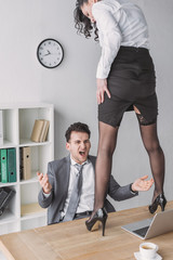 angry businessman screaming while looking at sexy secretary standing on desk in high heeled shoes