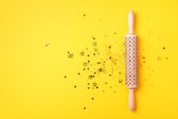 Rolling pin, gold glitter stars on yellow background. Top view. Copy space. Christmas baking concept. Holidays composition. Banner for menu, recipe, ingredients