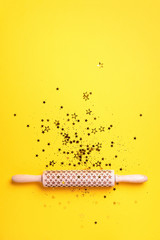 Rolling pin, gold glitter stars on yellow background. Top view. Copy space. Christmas baking concept. Holidays composition. Banner for menu, recipe, ingredients