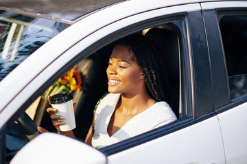 Smiling pretty young woman drinking take out coffee when driving to work in the morning