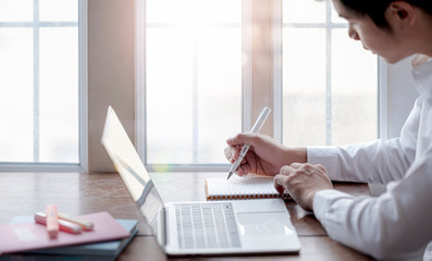 Young asian man writing and working with laptop at home.