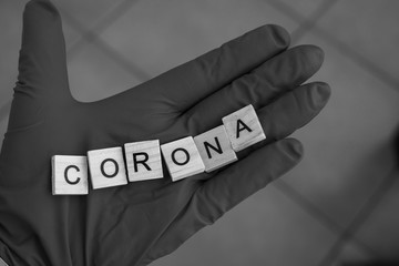  hand with a glove on holds Scrabble bricks, which form the word: Corona