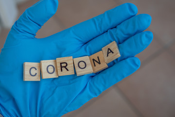  hand with a glove on holds Scrabble bricks, which form the word: Corona