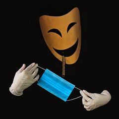 Hand-made theatrical mask of joy, with hands in medical gloves holding a blue medical mask. The...