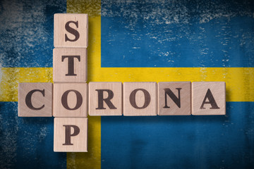 Fototapeta premium Flag of Sweden with wooden cubes spelling STOP CORONA on it. 2019 - 2020 Novel Coronavirus (2019-nCoV) concept art, for an outbreak occurs in Sweden.