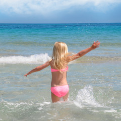 happy child girl on a tropical beach ocean has a fun with splash. Summer vacation concept