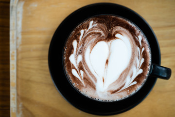 Latte art in heart shape with a cup of dark chocolate on wooden table