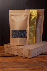 Paper and foil pouch bags with coffee beans and tea leaves on dark wooden background. Packaging for foods and goods brand mockup, shopping offer, sales. Weight products packs with clasps and windows.