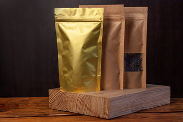 Paper and foil pouch bags with coffee beans and tea leaves on dark wooden background. Packaging for foods and goods brand mockup, shopping offer, sales. Weight products packs with clasps and windows.