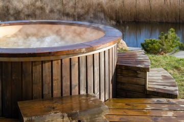 How water swirling in wooden hot tub outside in nature. Enjoying hot steaming pool on a sunny day, private spa treatment. Nobody - obrazy, fototapety, plakaty