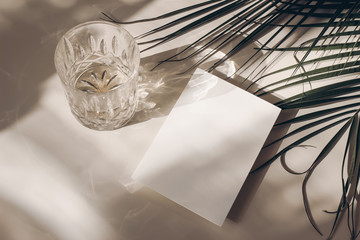 Summer tropical stationery still life scene. Glass of water, palms leaves. Beige table background...