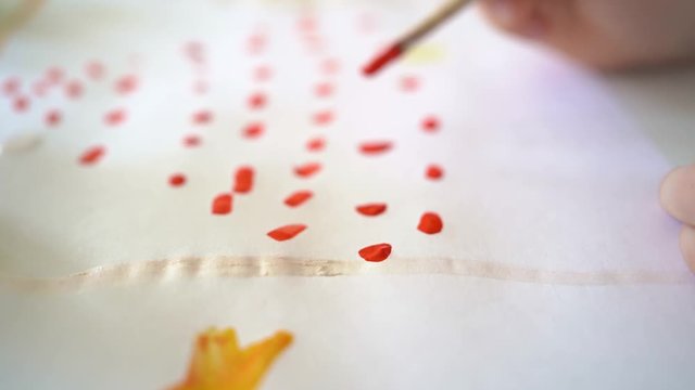 children hand draws red point on a sheet. close up