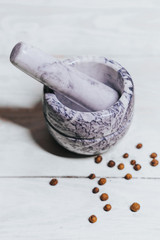 Stone white mortar and dried herbs, pepper, coriander ona a white wooden background table.