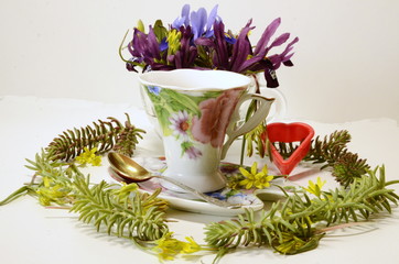 On a white background, a cup of coffee and a composition with fresh spring wildflowers.