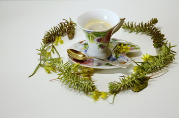 On a white background, a cup of coffee and a composition with fresh spring wildflowers.