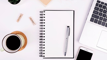 White office table with blank notebook with pen and mock up. Laptop, cup of coffee, phone and wooden accessories. Business desk and empty document to write.