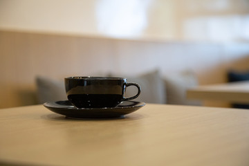 A black cup of coffee placed on a wooden table by the window in a coffee shop, Concept: Delicious breakfast drinks fragrant suitable for lifestyle, closeup cup of coffee over the top with space