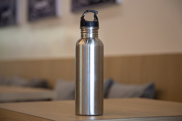 Aluminum bottle water placed on a wooden table in a restaurant or  shop, Concept: Reduce plastic waste to recycle reusable and ecology nature,  stainless glossy metal-containing liquid for sport