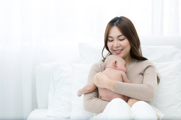 Beautiful mom supports and tenderly cuddles the newborn baby gently while the infant is sleeping on the chest. Asian mother looking at the baby with love and showing protection.