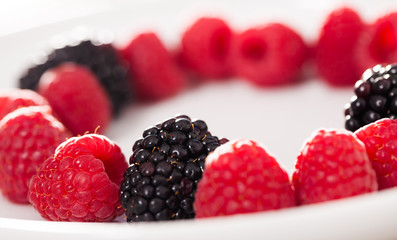 raspberries and blackberries laid out on a white plate in circle