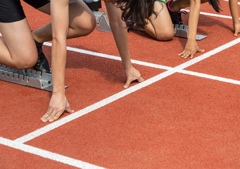 Female athletes preparing for race hands on starting line blocks in the running track at stadium