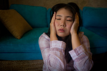 young beautiful sad and depressed Asian Korean woman in pajamas at home sitting by living room couch feeling unhappy and confused suffering broken heart