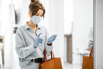 Woman in medical mask and gloves disinfecting hands after coming home from the street. Concept of...