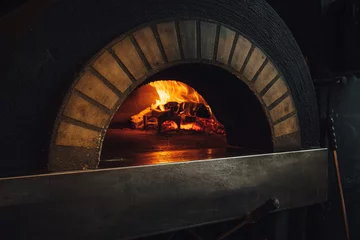 Tuinposter Dark brick pizza oven with fire in restaurant © Aleksandrs Muiznieks