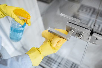 Woman in protective gloves disinfecting door handle while cleaning at home, close-up view on hands