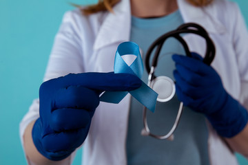 Doctor holding blue awareness ribbon, closeup view. Symbol of medical issues