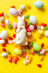 Happy Easter concept. Preparation for holiday. Easter candy chocolate eggs bunny and jellybean sweets isolated on trendy yellow background. Simple minimalism flat lay top view copy space.