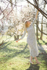 A young woman walks among blossoming apricot trees.